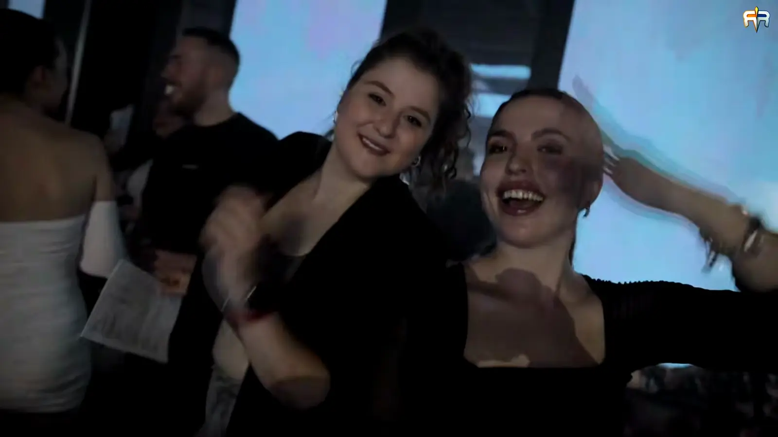 Dve devojke plešu i smeju se u ljubičastom svetlu