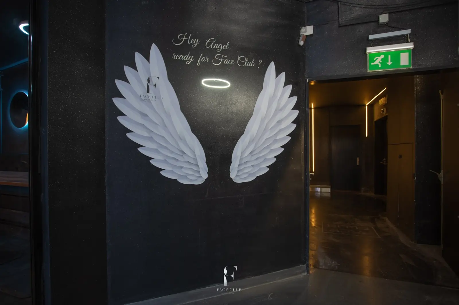 Ulaz u Face Club: bela anđeoska krila na crnom zidu i natpis „Hey Angel, ready for Face Club?“